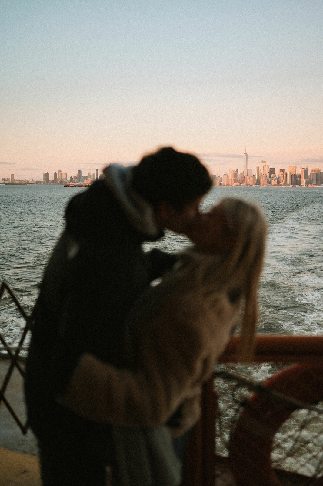 Baiser flou au premier plan sur le pont d'un ferry, la skyline de Manhattan et le One World Trade Center nets au coucher du soleil