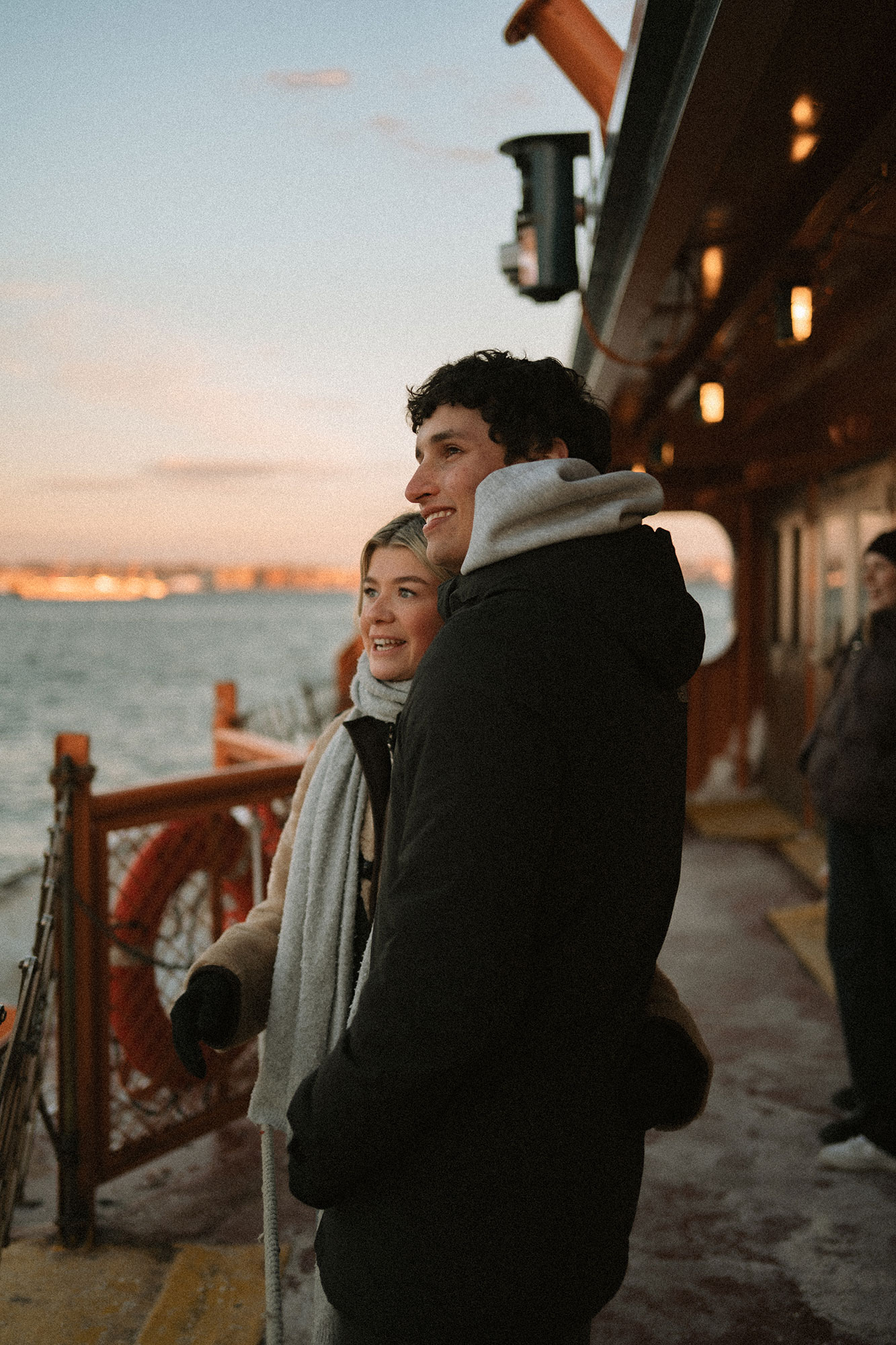 Couple souriant qui regarde l'horizon sur le pont d'un ferry à New York, bastingage orange et lumière de fin de journée