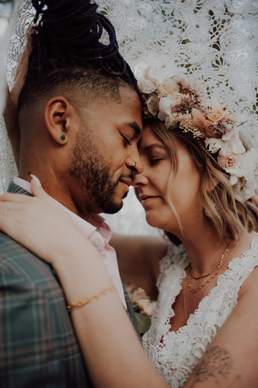 Shooting inspiration mariage bohème : mariés front contre front sous un voile de dentelle, elle coiffée d'une couronne de fleurs