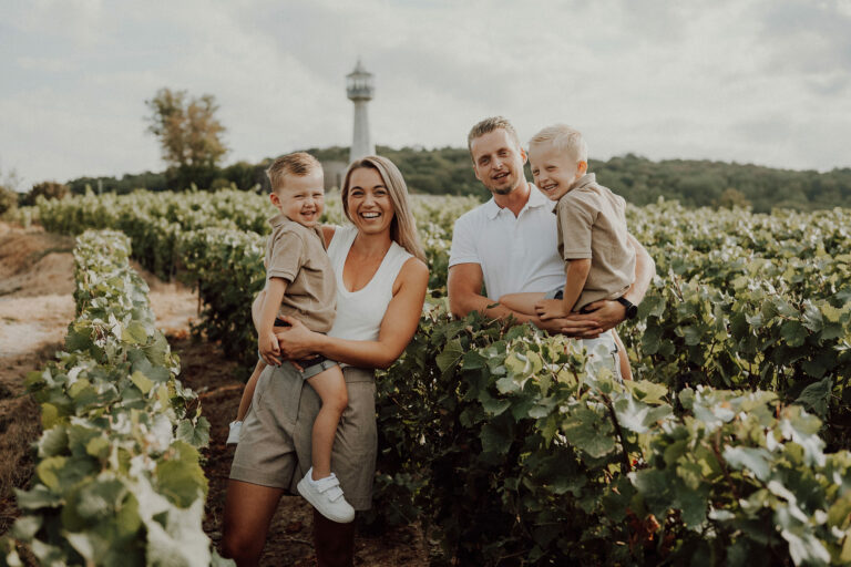 Portrait de famille dans les rangs de vigne, chaque parent porte un petit garçon, phare de Verzenay en arrière-plan